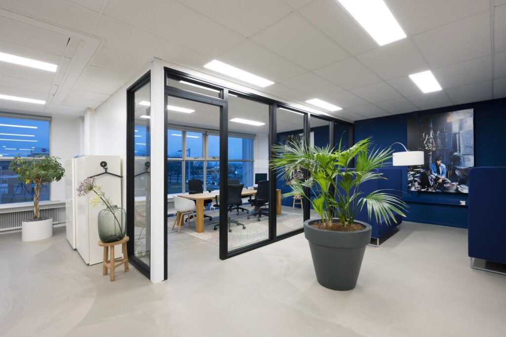 Modern kantoorinterieur aan de Van der Madeweg met glazen vergaderruimte, planten en blauwe accenten.